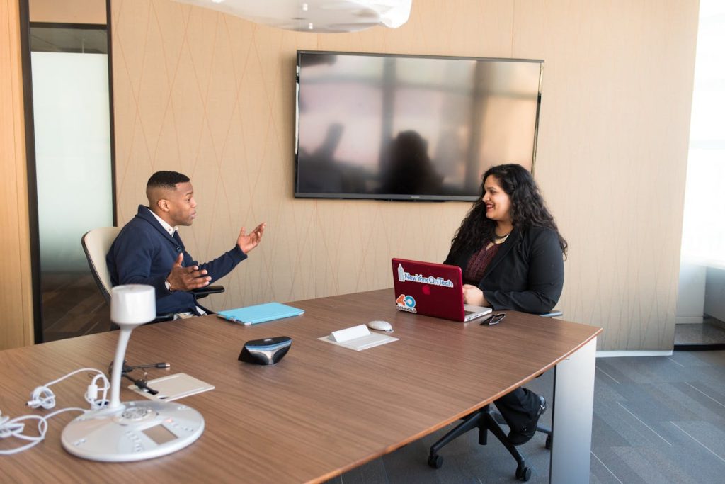man-wearing-black-suit-1181377 Two professionals discussing in a modern office with laptops and smart technology.